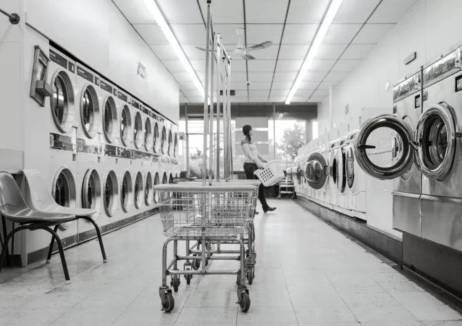 a-woman-is-carrying-a-laundry-basket-inside-the-coin-laundry-shop-Post-Featured-Image